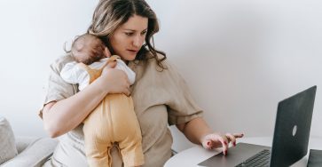 young working mother cuddling baby and using laptop at home